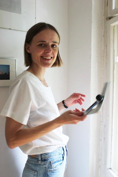 Eine Frau steht bei der Einrichtungsberatung neben einem Altbaufenster und hält ein Messwerkzeug in der Hand. Sie lächelt in die Kamera.